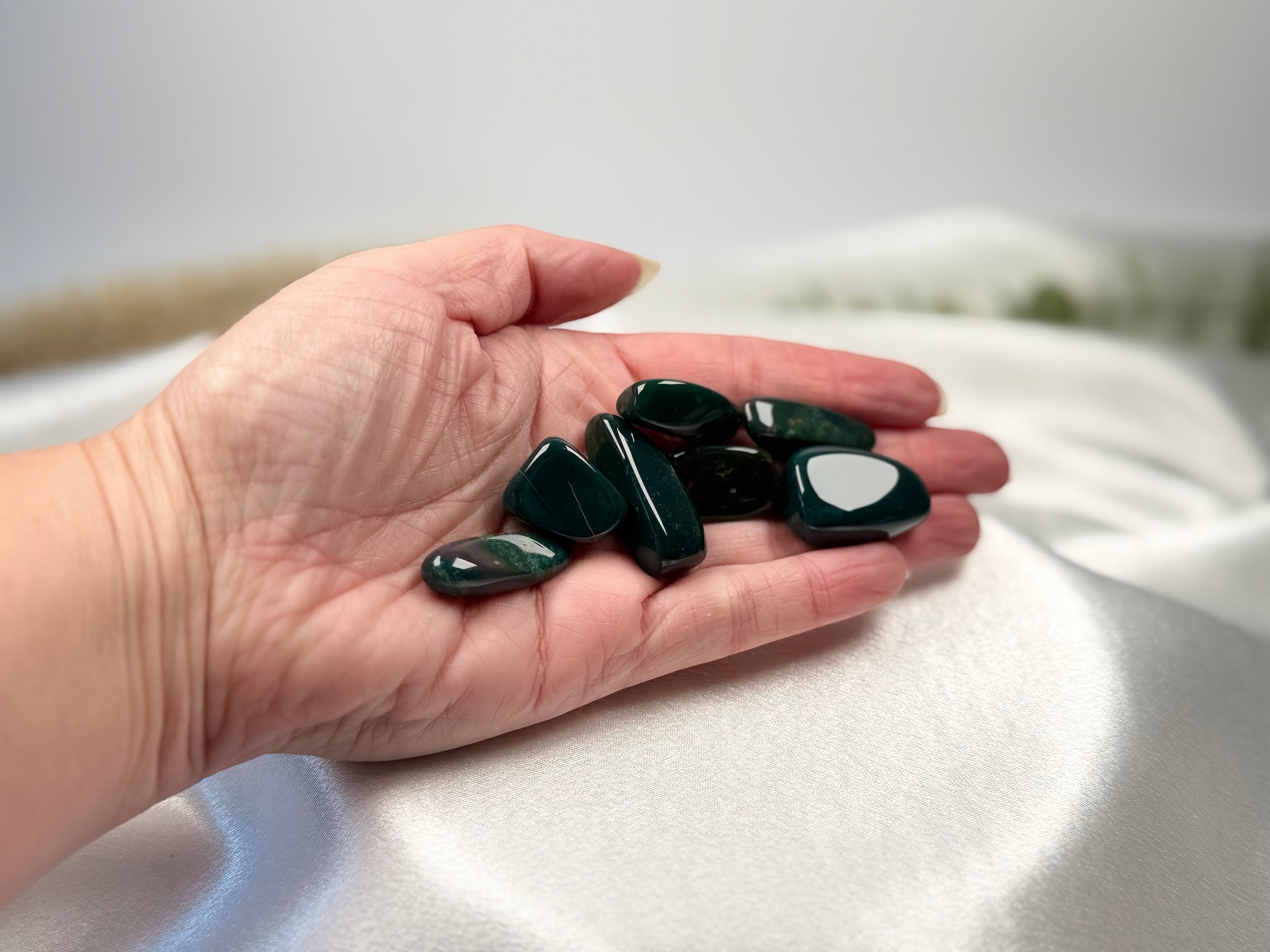 Treasured Energies polished bloodstone tumbled gemstones held in a palm against a soft white fabric background.