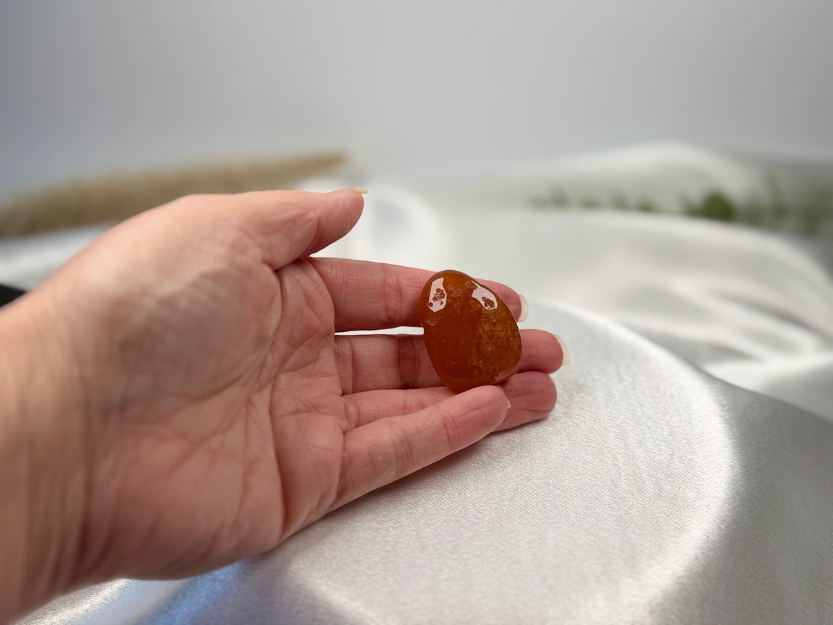 Treasured Energies polished carnelian stone tumbled gemstone held in a palm against a soft white satin background