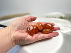 Treasured Energies polished carnelian stone tumbled gemstones held in a palm against a soft white satin background