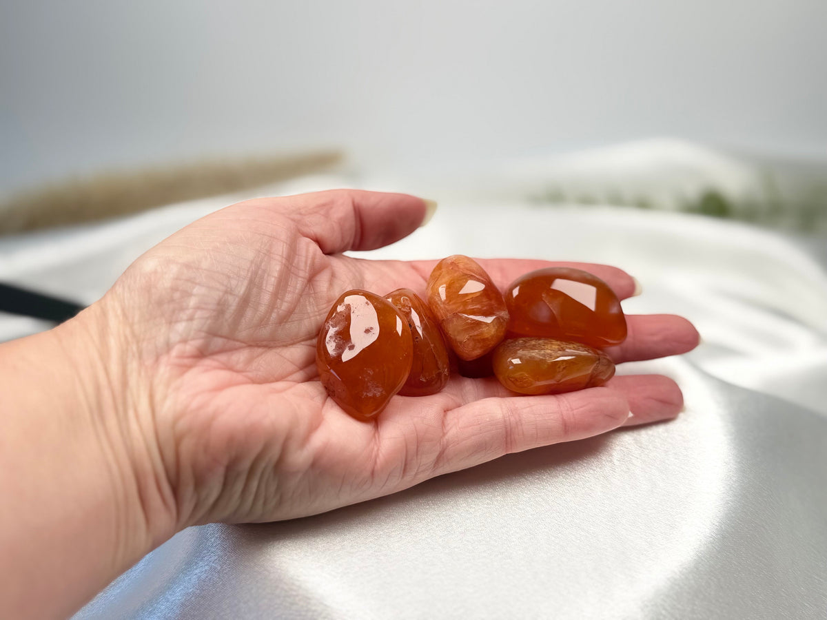 Treasured Energies polished carnelian stone tumbled gemstones held in a palm against a soft white satin background