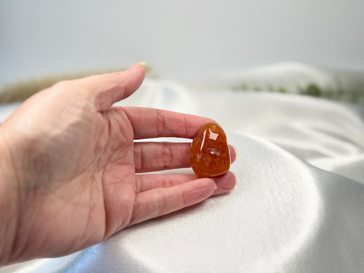 Treasured Energies polished carnelian stone tumbled gemstone held in a hand against a soft white satin background