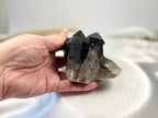 Treasured Energies raw smoky quartz crystal cluster held in a hand, showing deep grey and brown natural points.