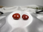 Two polished heart-shaped Red Jasper crystals from Treasured Energies resting on white satin fabric.