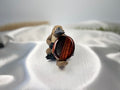 Treasured Energies red tiger's eye worry stone held by a small platypus figurine on a white satin background.