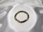 Treasured Energies natural rhyolite beaded elastic bracelet with earthy green and brown tones on a silk background