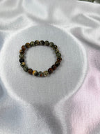 Treasured Energies natural rhyolite beaded elastic bracelet with earthy green and brown tones on white satin fabric