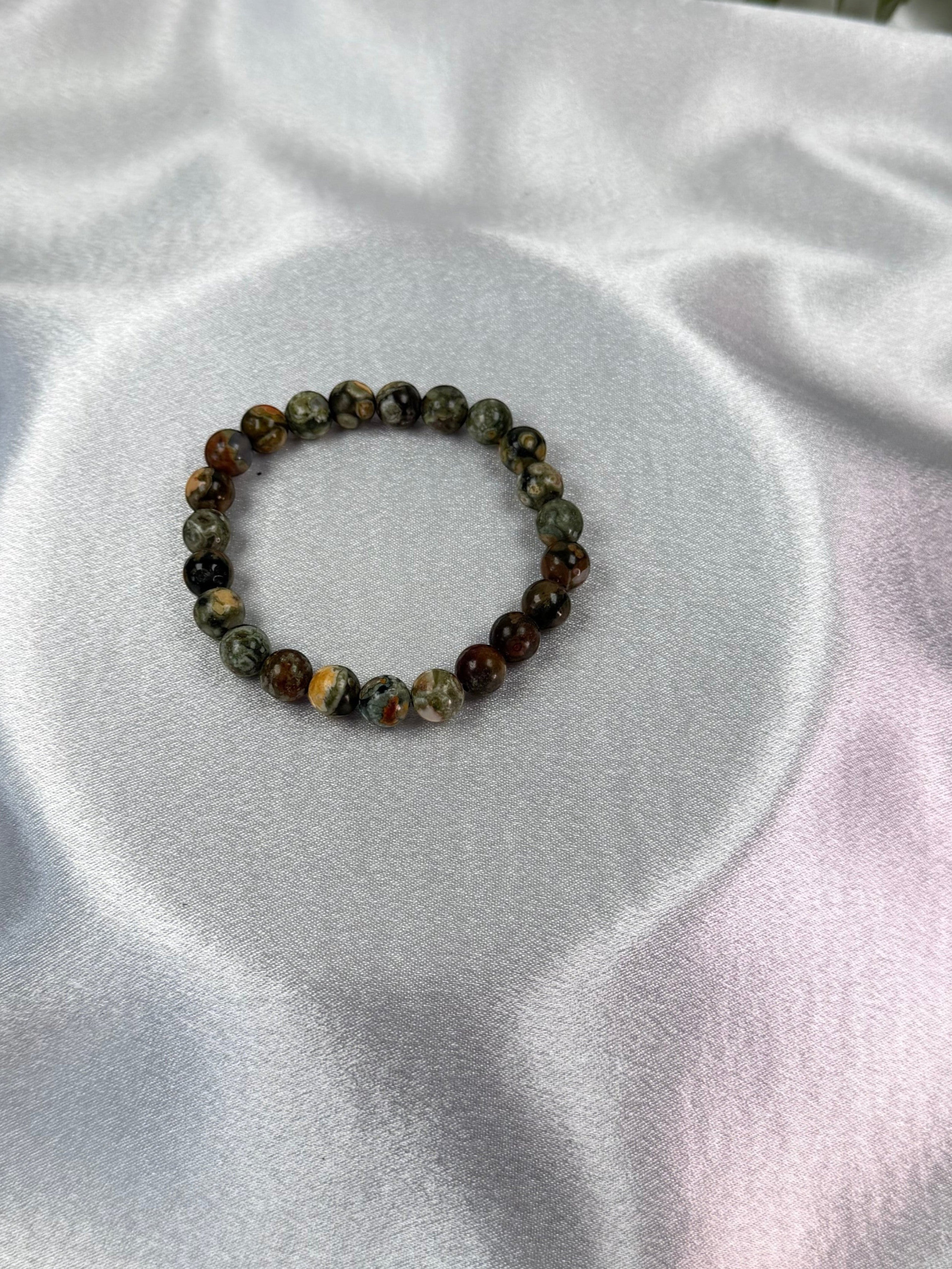 Treasured Energies natural rhyolite beaded elastic bracelet with earthy green and brown tones on white satin fabric