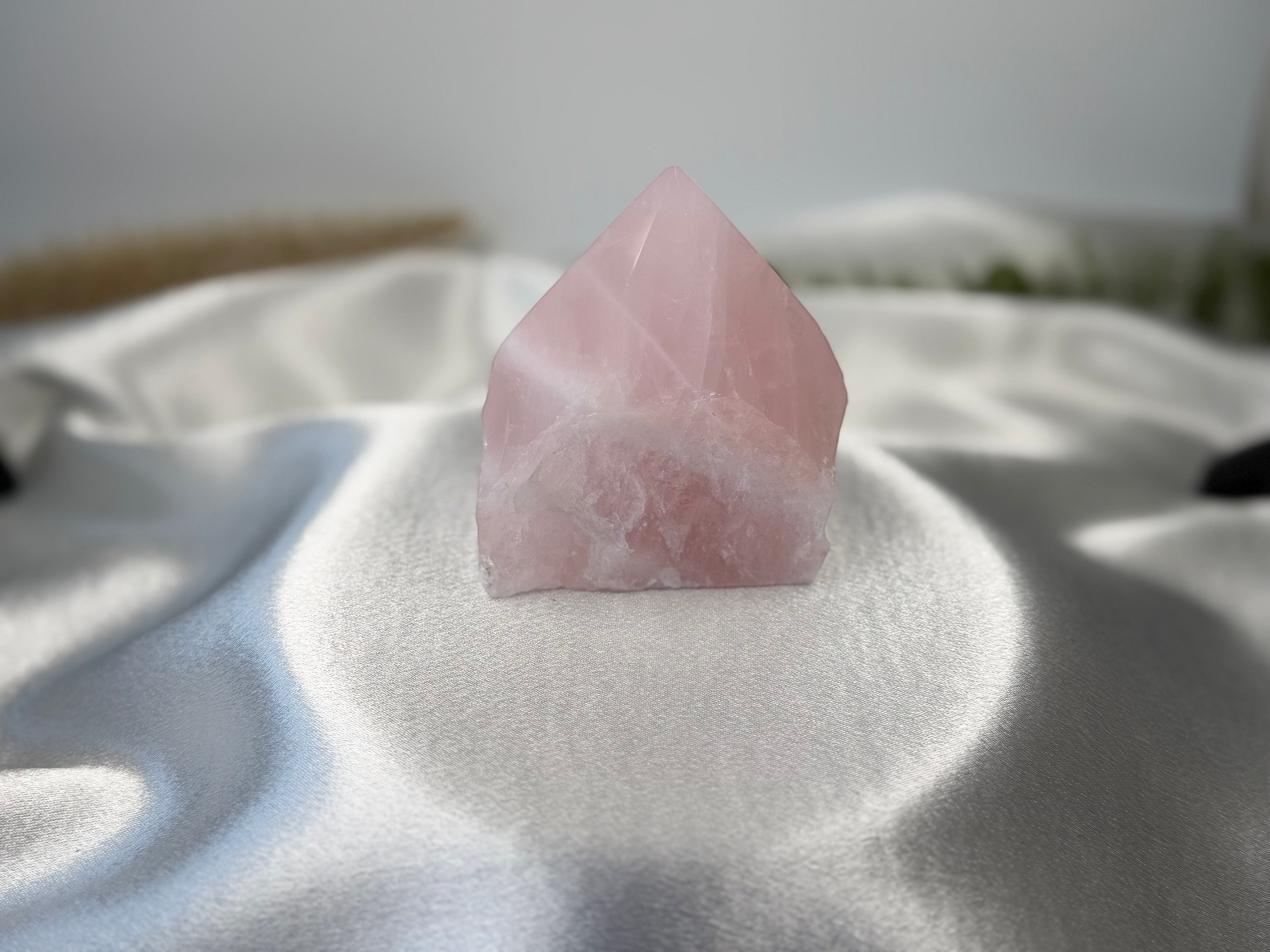 Treasured Energies polished rose quartz crystal point with a raw base resting on a soft white satin fabric.