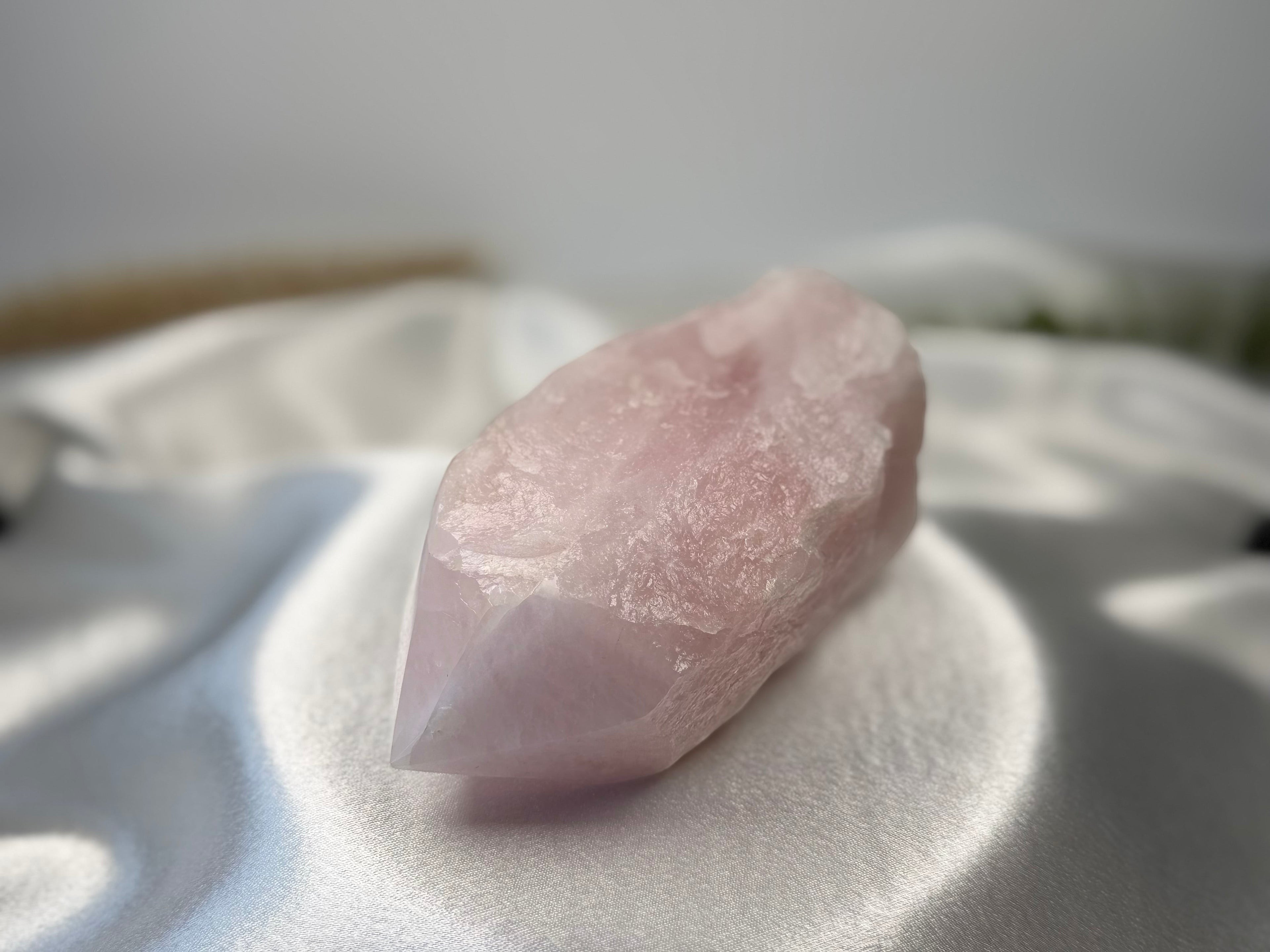 Treasured Energies large rose quartz crystal point with a polished tip and raw base resting on white satin fabric.