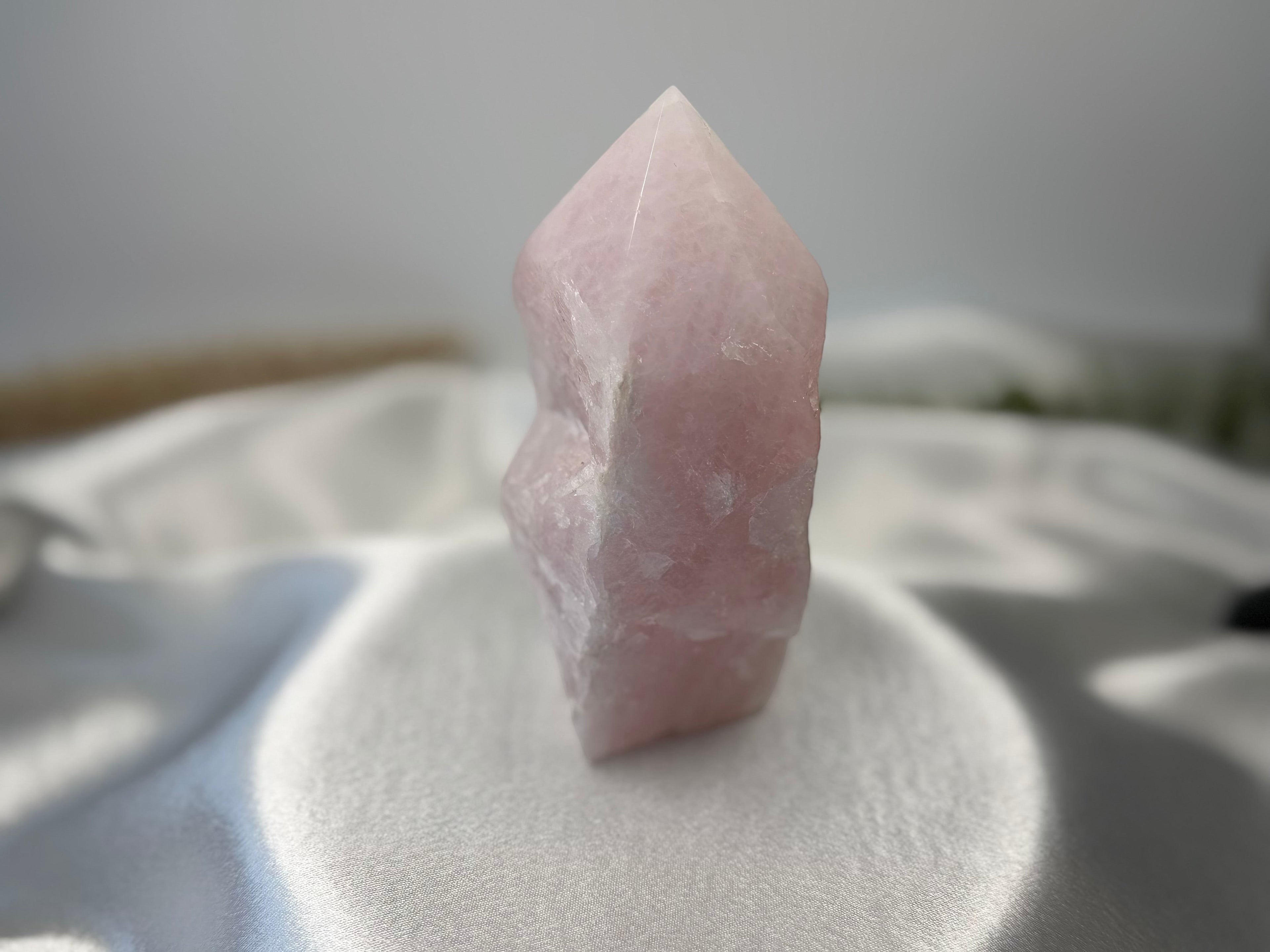 Treasured Energies large rose quartz crystal point with a polished tip and raw base on a white satin fabric background