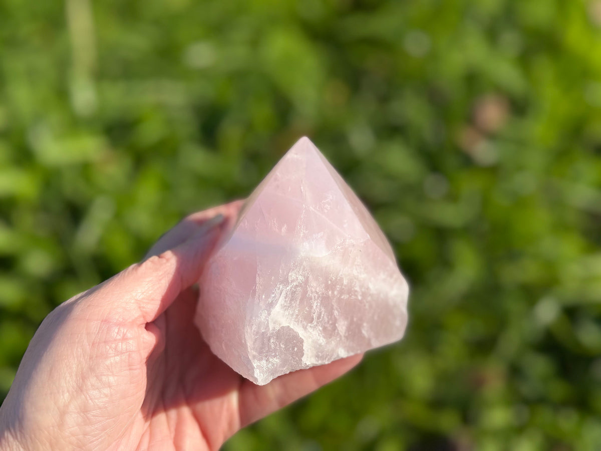 Treasured Energies medium rose quartz crystal point with a polished tip and raw base held in a hand outdoors.