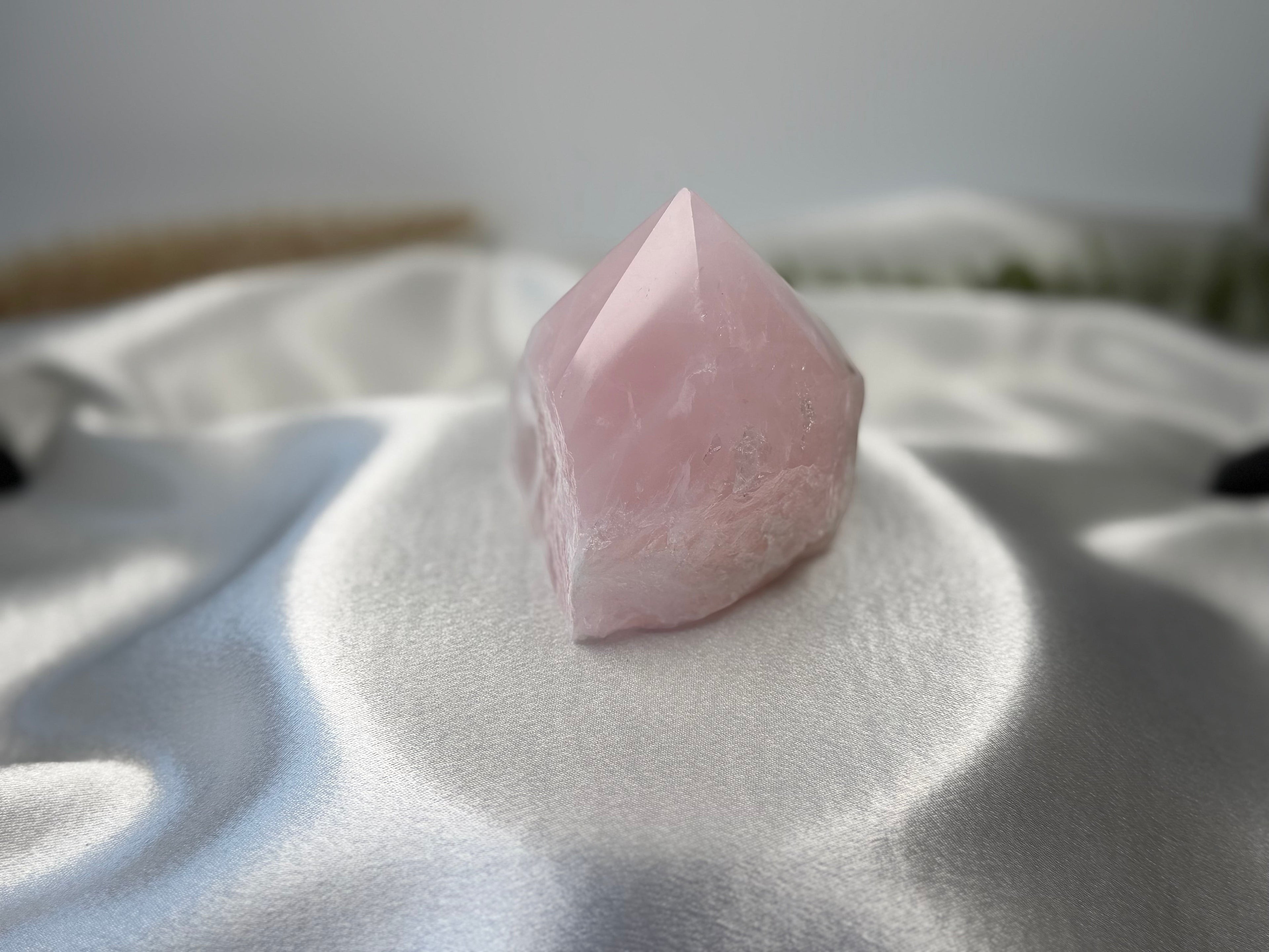 Treasured Energies medium rose quartz crystal tower with a polished point and raw base on a white satin fabric.