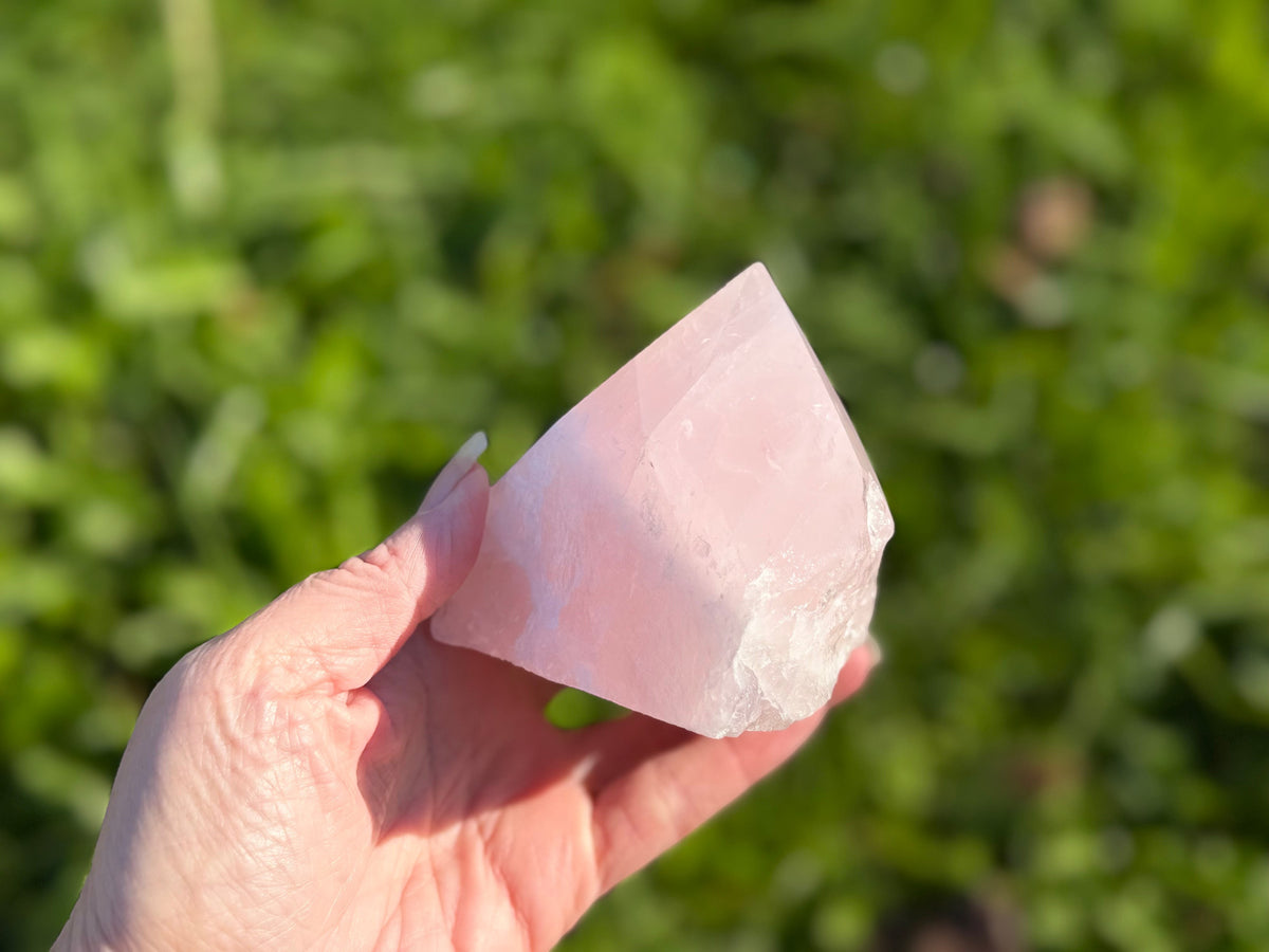 Treasured Energies medium rose quartz crystal point with a polished top and raw base held in a hand outdoors.