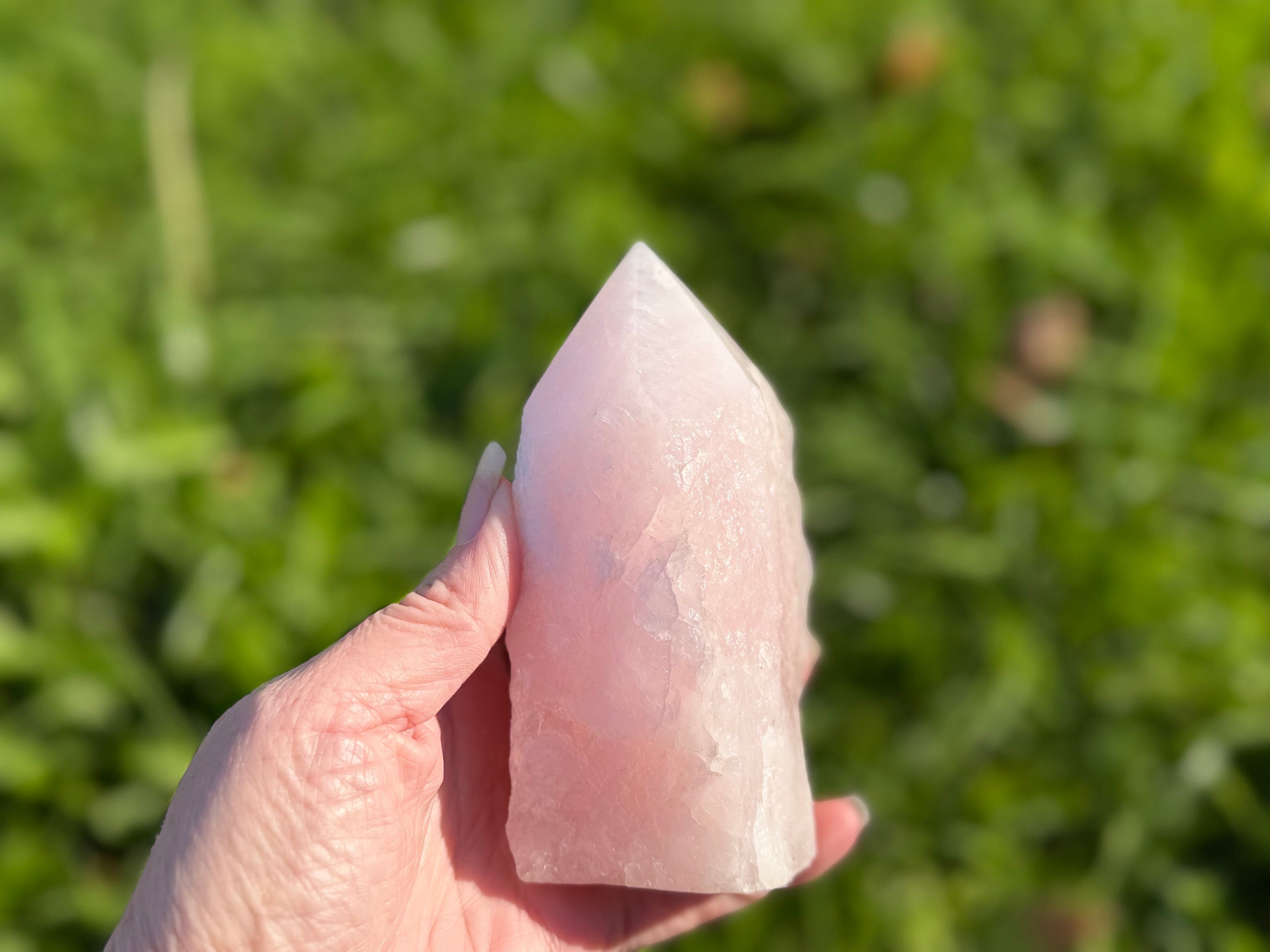 Treasured Energies large rose quartz crystal tower with a polished point and raw base held in a hand outdoors