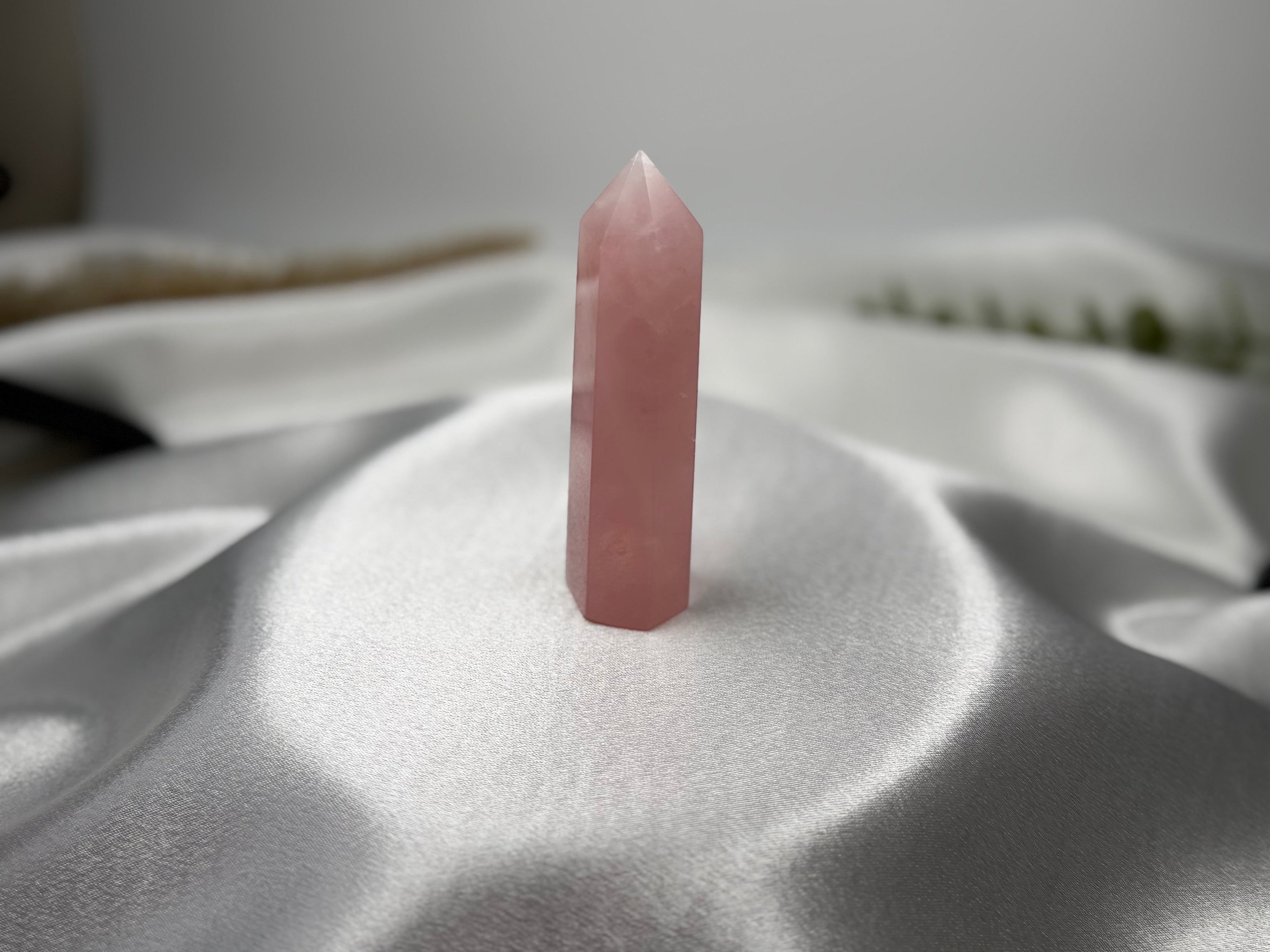 Treasured Energies polished rose quartz crystal tower standing on a smooth white satin fabric background.
