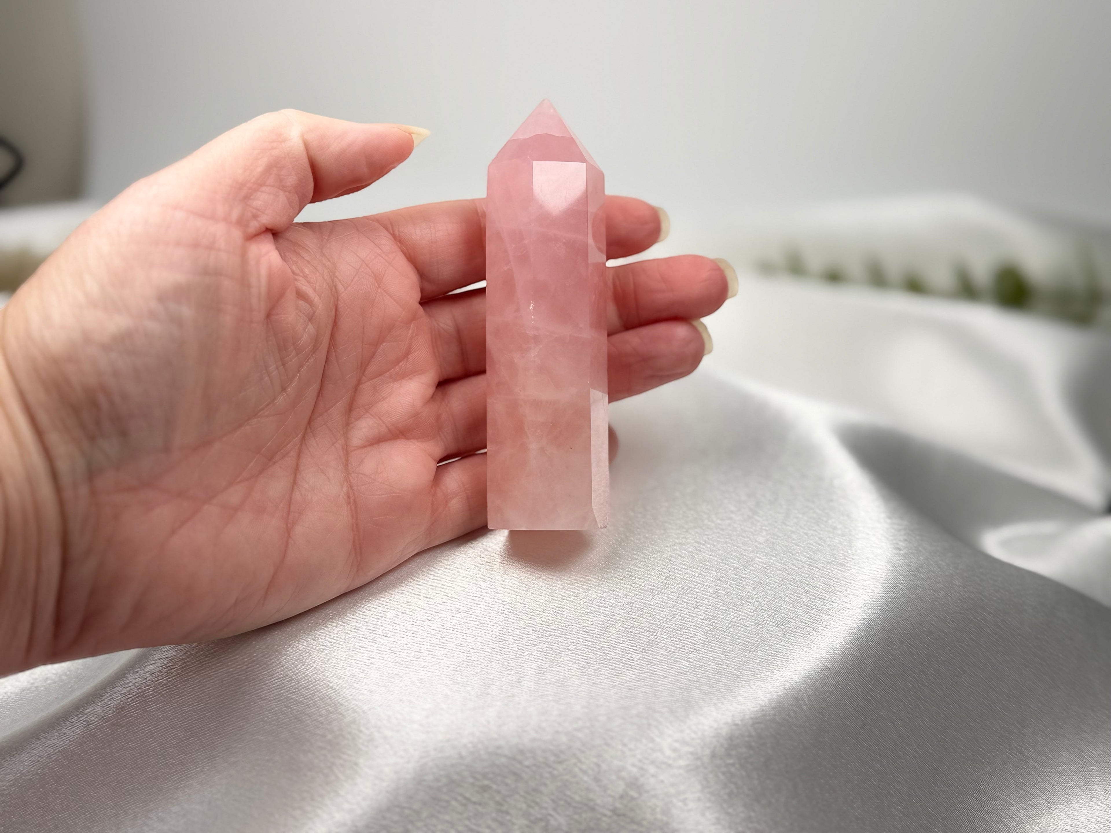Treasured Energies polished rose quartz crystal generator tower held in a hand against a white satin background.