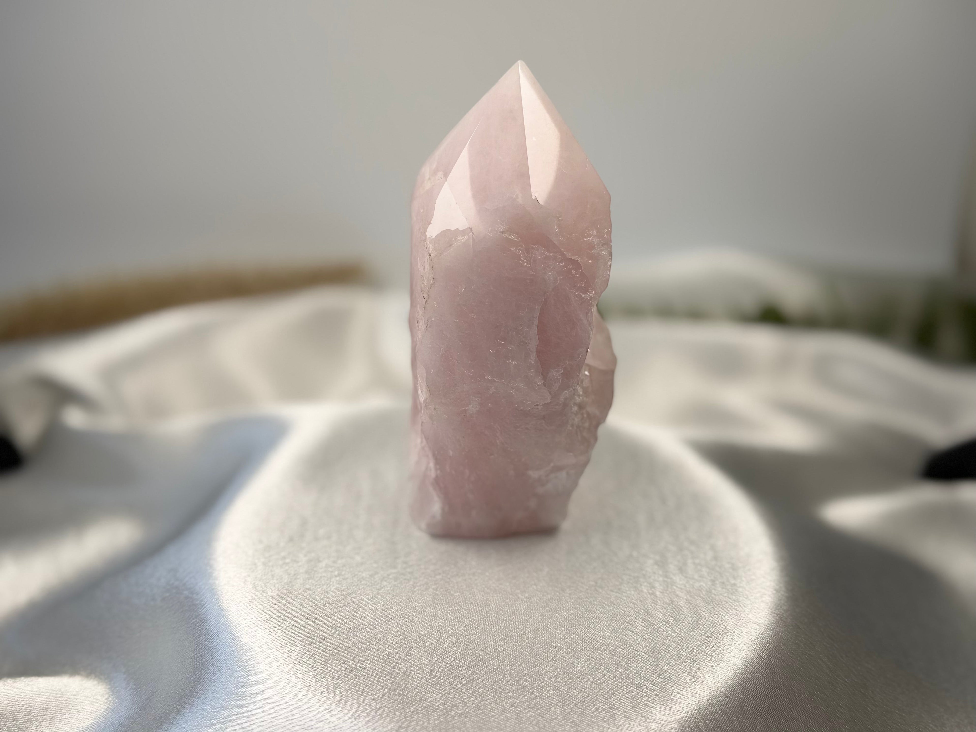Treasured Energies large rose quartz crystal tower with a polished point and raw base on a white satin cloth