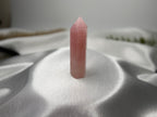 Treasured Energies polished rose quartz crystal tower with a pointed tip on a white satin background.