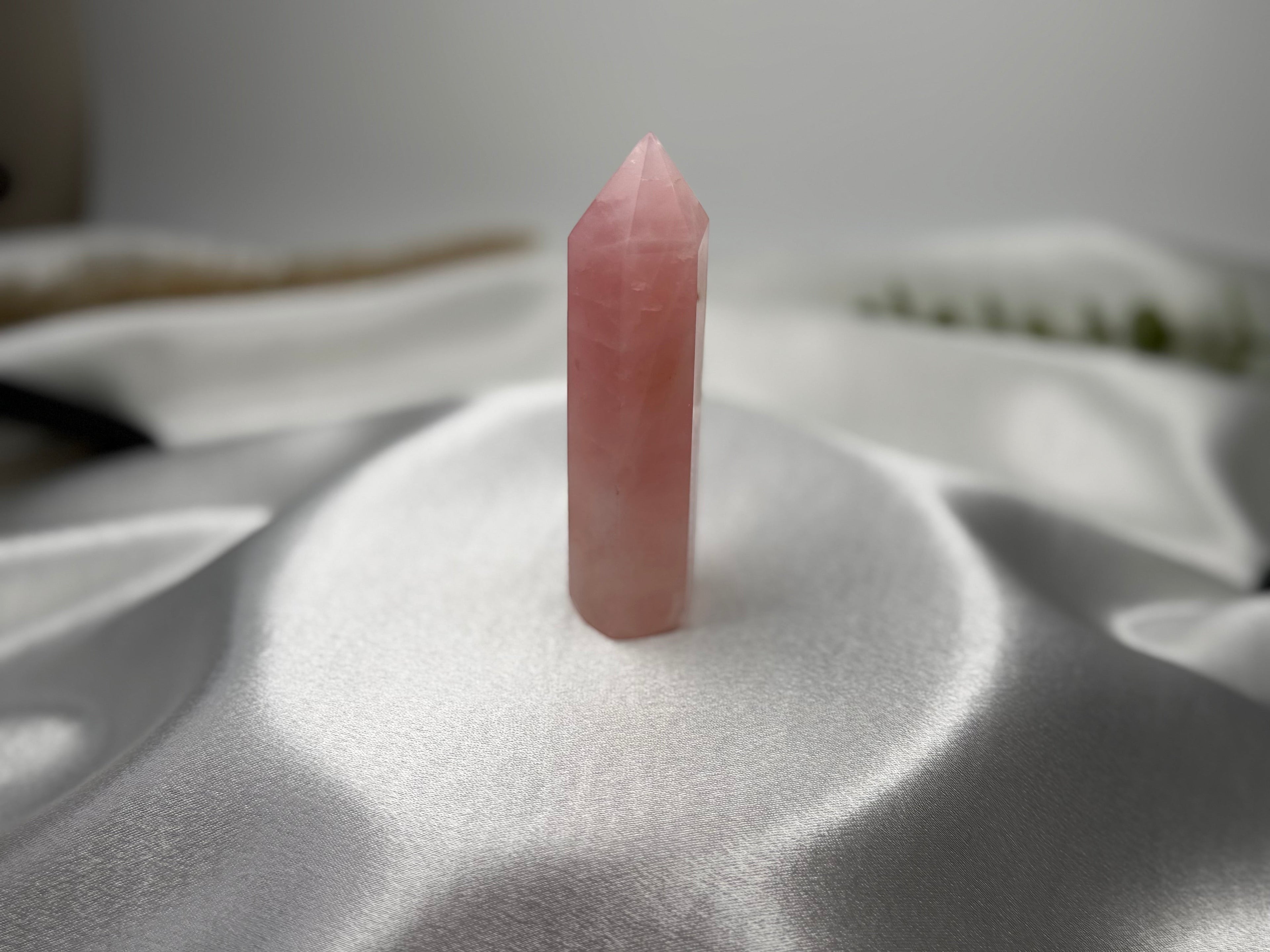 Treasured Energies polished rose quartz crystal tower with a pointed tip on a white satin background.