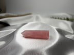 Treasured Energies polished rose quartz crystal tower resting on soft white satin fabric