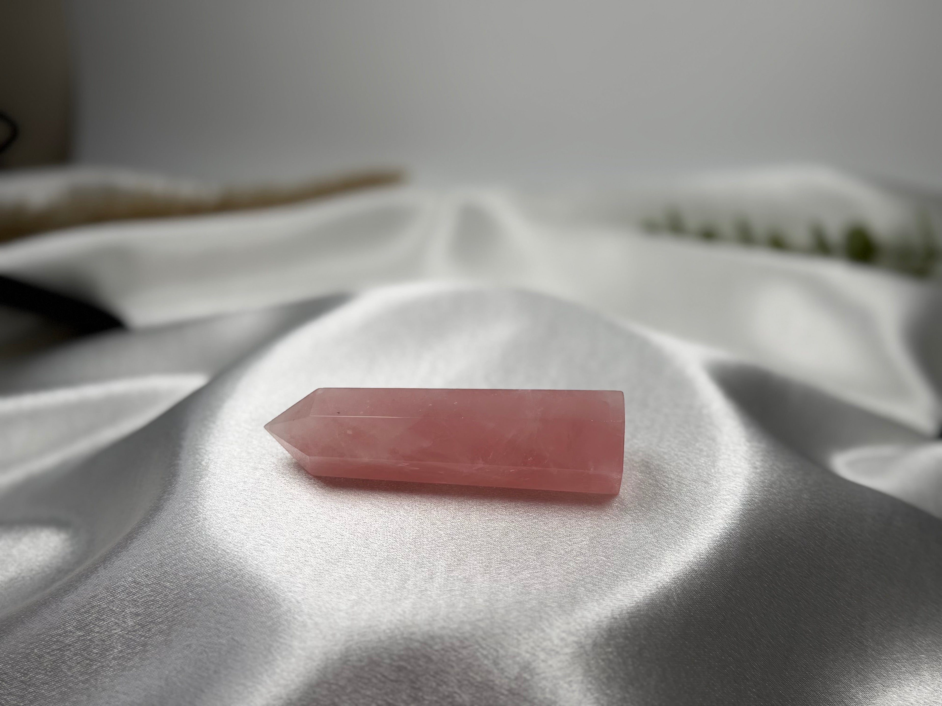 Treasured Energies polished rose quartz crystal tower resting on soft white satin fabric