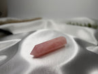 Treasured Energies polished rose quartz crystal tower with a pointed tip resting on a soft white satin fabric.