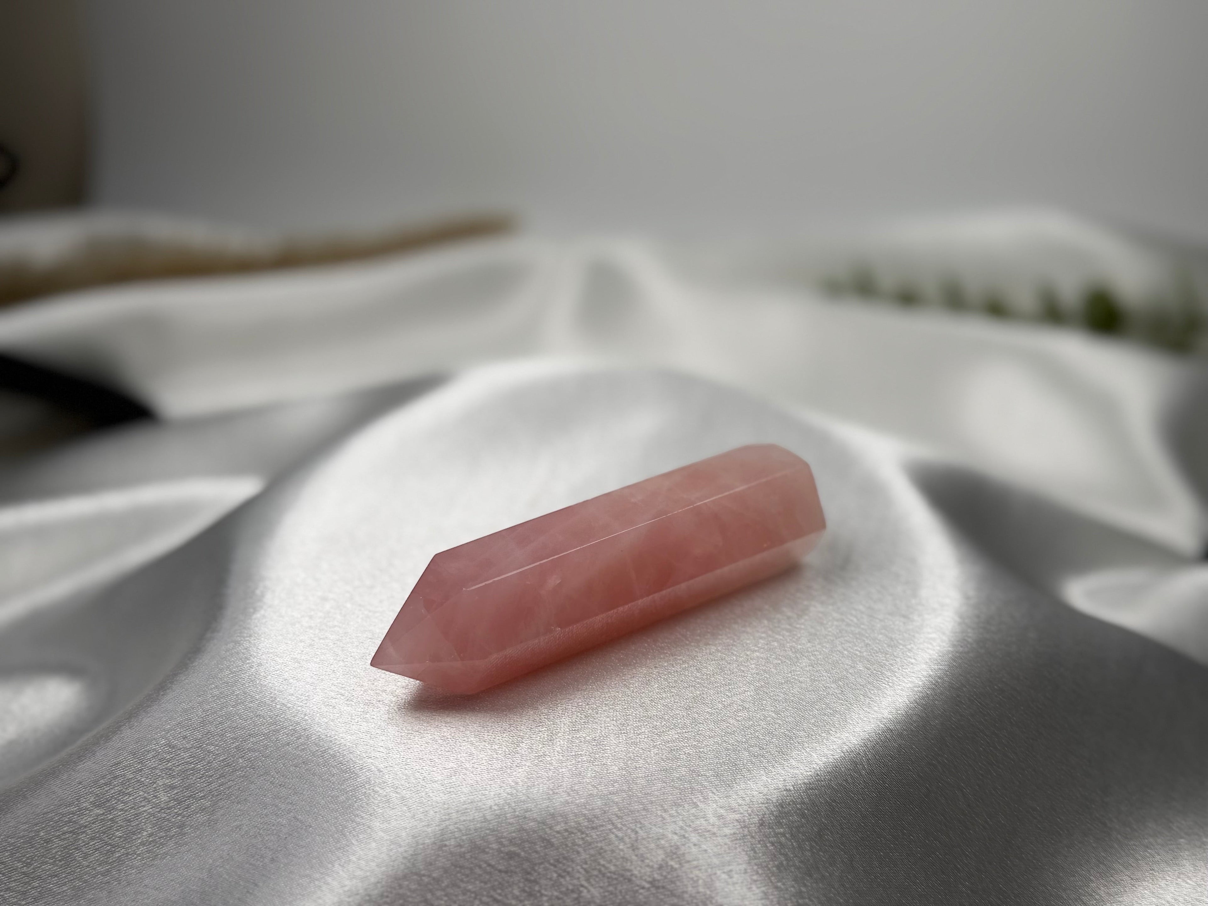 Treasured Energies polished rose quartz crystal tower with a pointed tip resting on a soft white satin fabric.