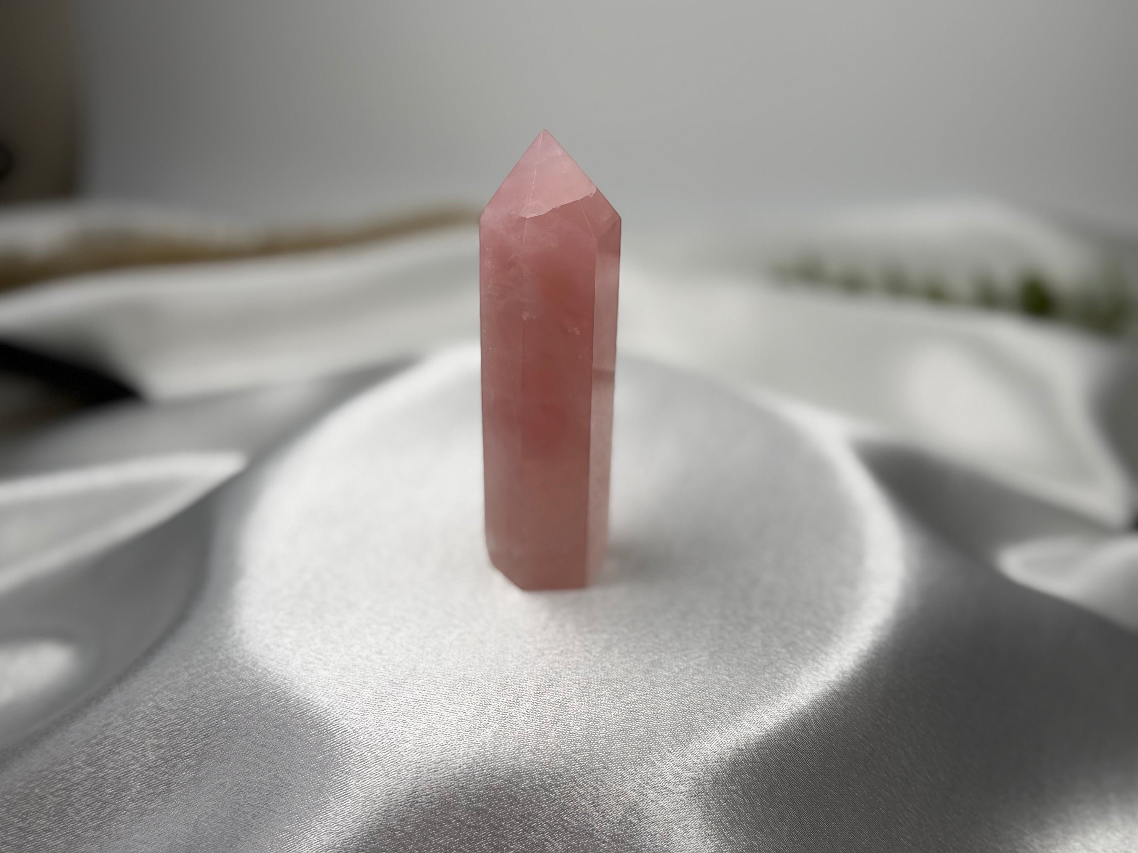 Treasured Energies polished rose quartz crystal tower generator with a pointed tip on a soft white satin background.