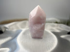 Treasured Energies large rose quartz crystal tower with a polished point and raw base on a white satin fabric background
