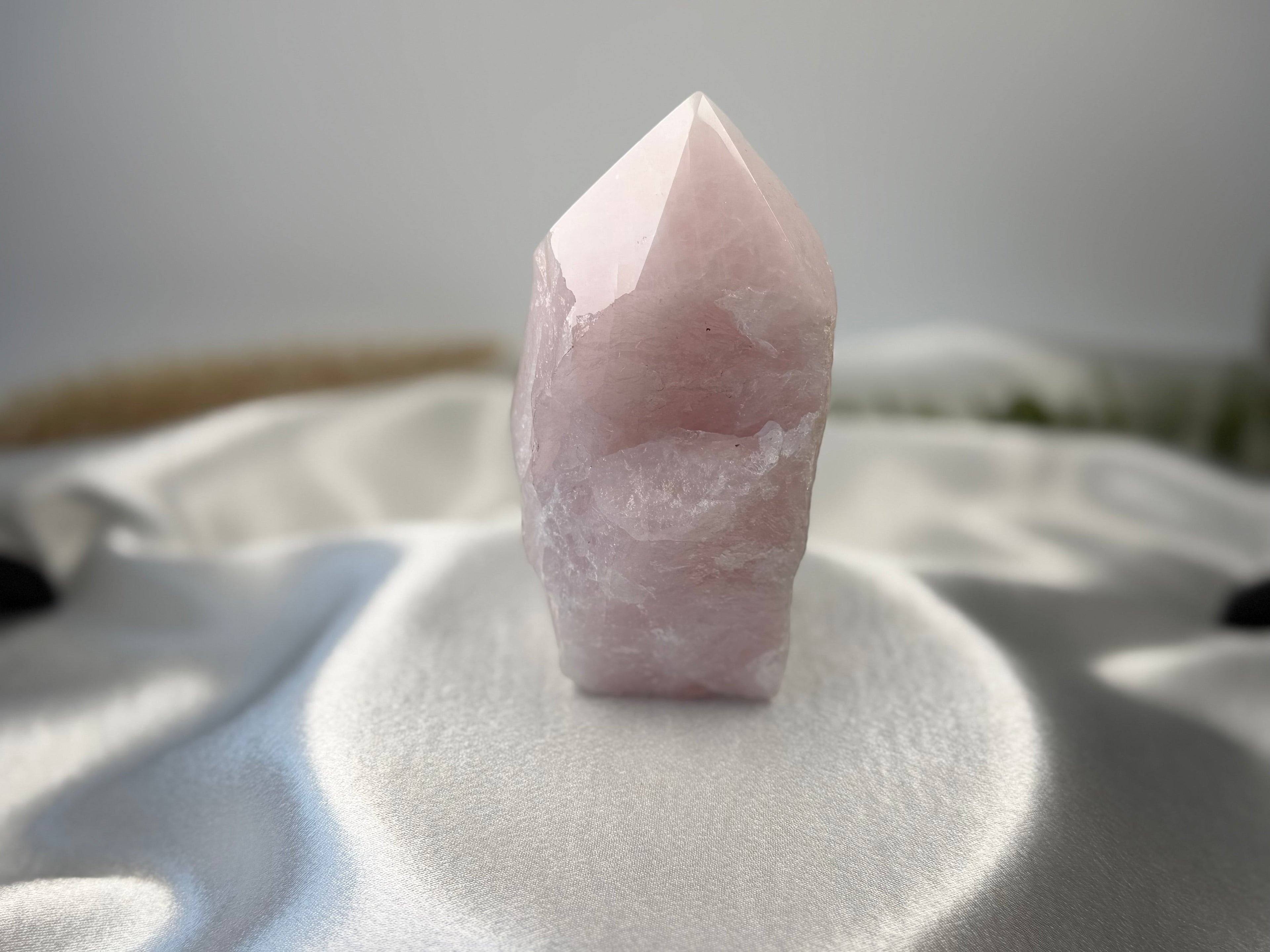 Treasured Energies large rose quartz crystal tower with a polished point and raw base on a white satin fabric background