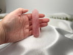 Treasured Energies polished rose quartz crystal tower held in a hand against a soft white satin background.