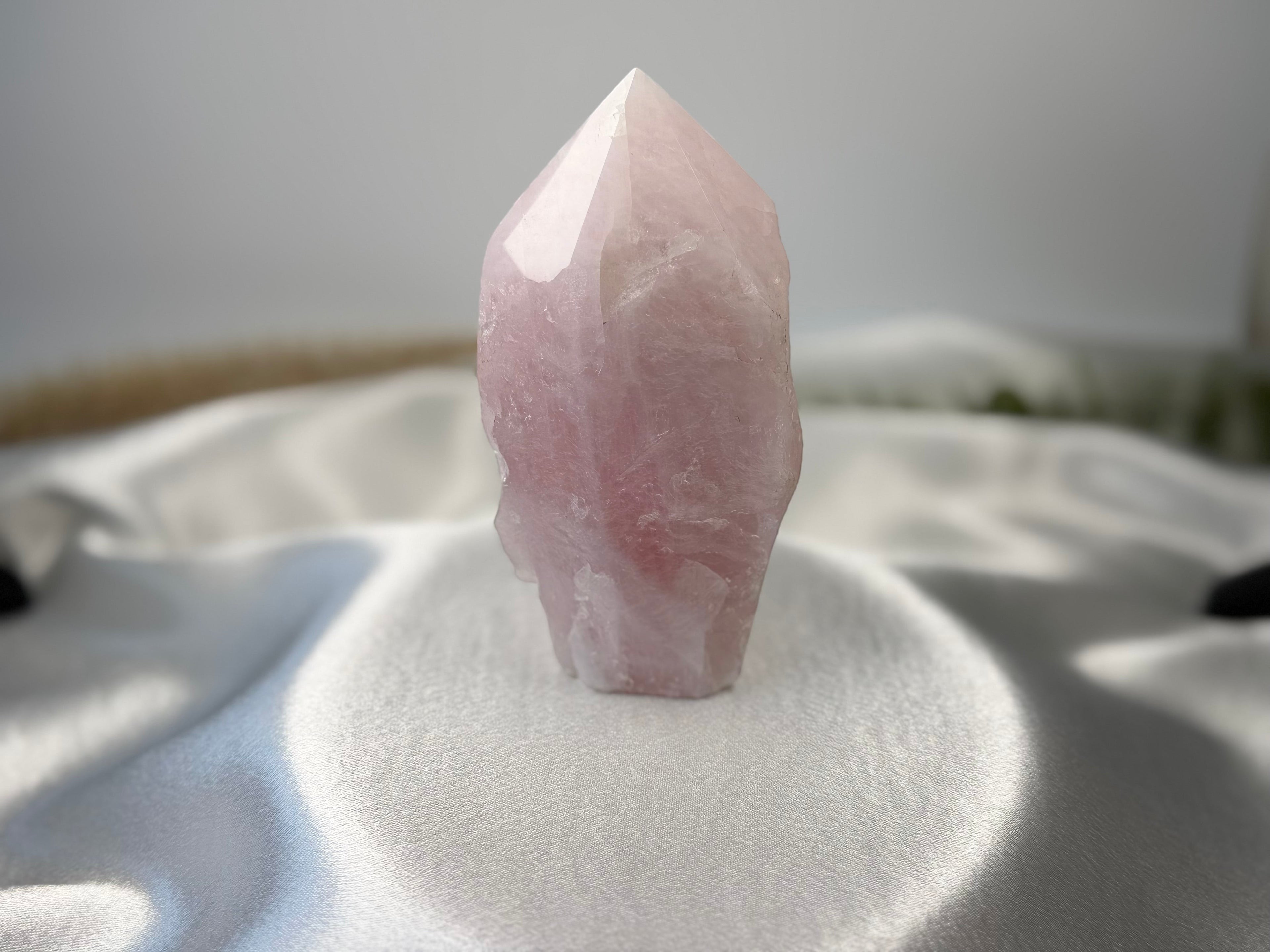 Treasured Energies large rose quartz crystal tower with a polished point and raw base on a white satin fabric