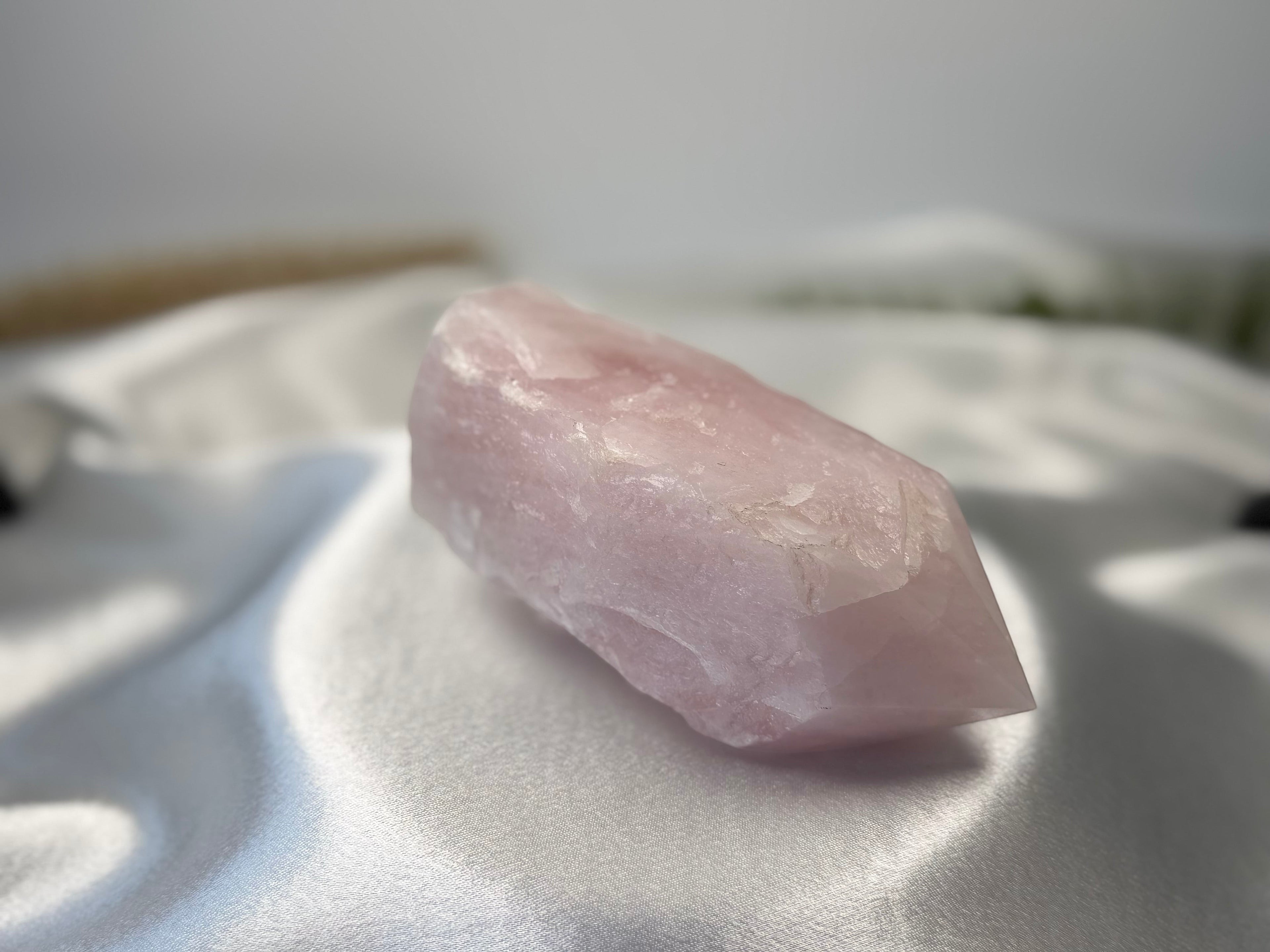 Treasured Energies large rose quartz crystal tower with a polished point resting on a soft white satin fabric