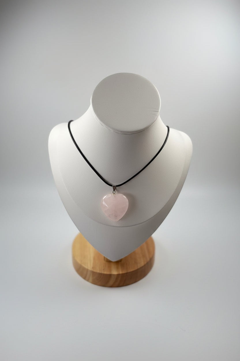 Treasured Energies heart-shaped rose quartz crystal pendant on a black cord necklace displayed on a white mannequin bust.