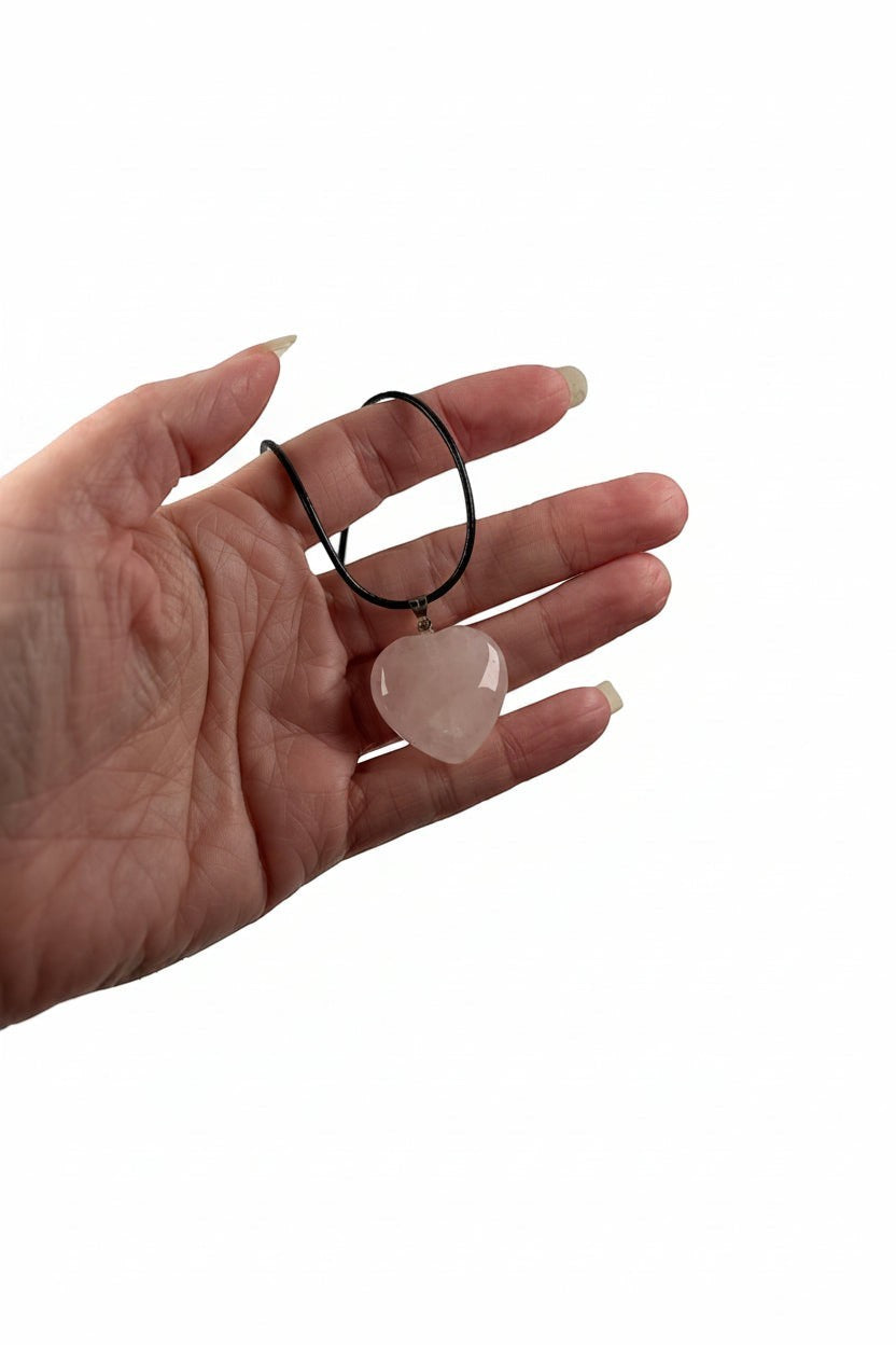 Treasured Energies heart-shaped rose quartz crystal pendant on a black cord necklace held in a hand