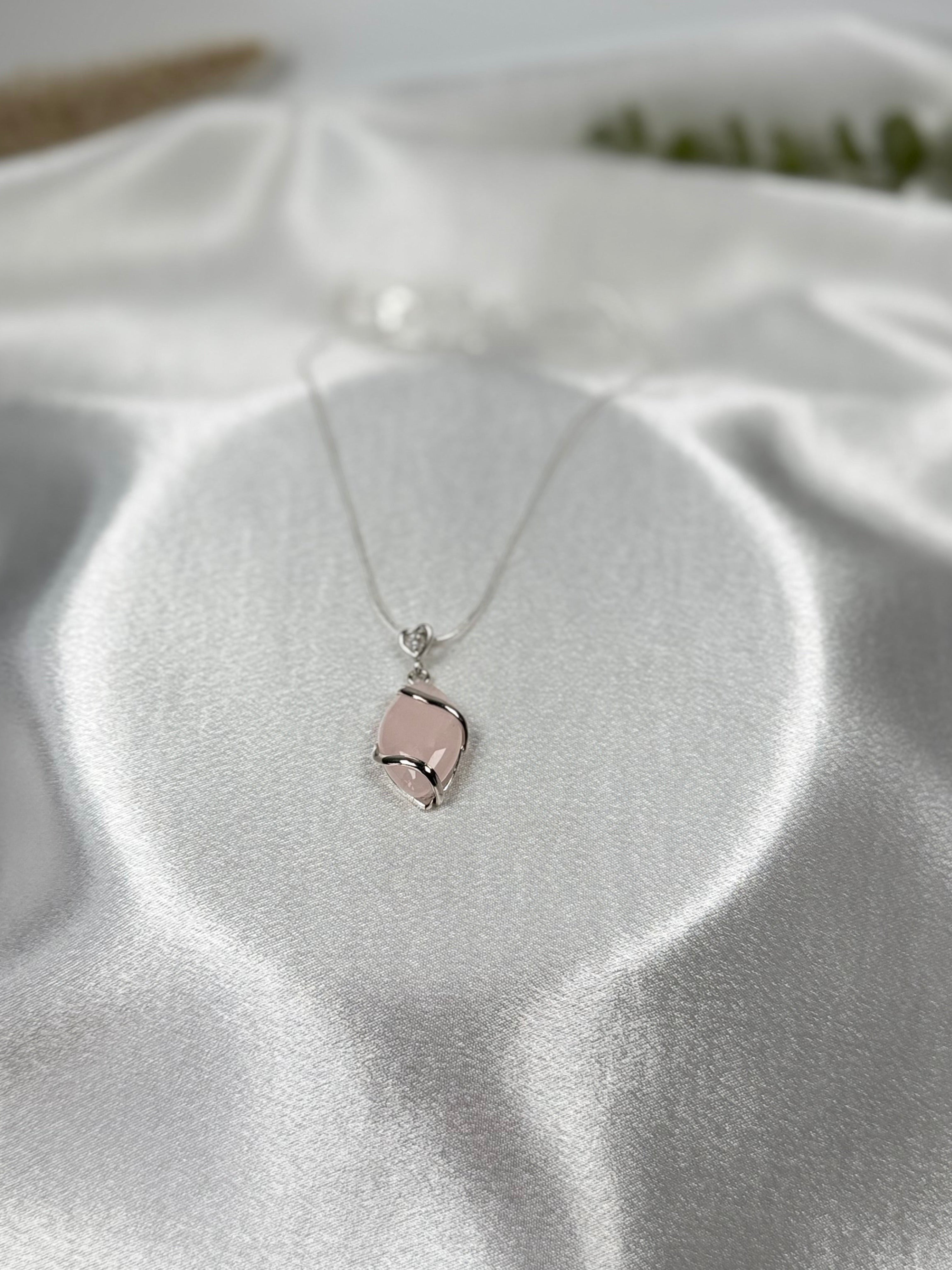 Treasured Energies rose quartz crystal pendant necklace with a silver setting on a white satin background