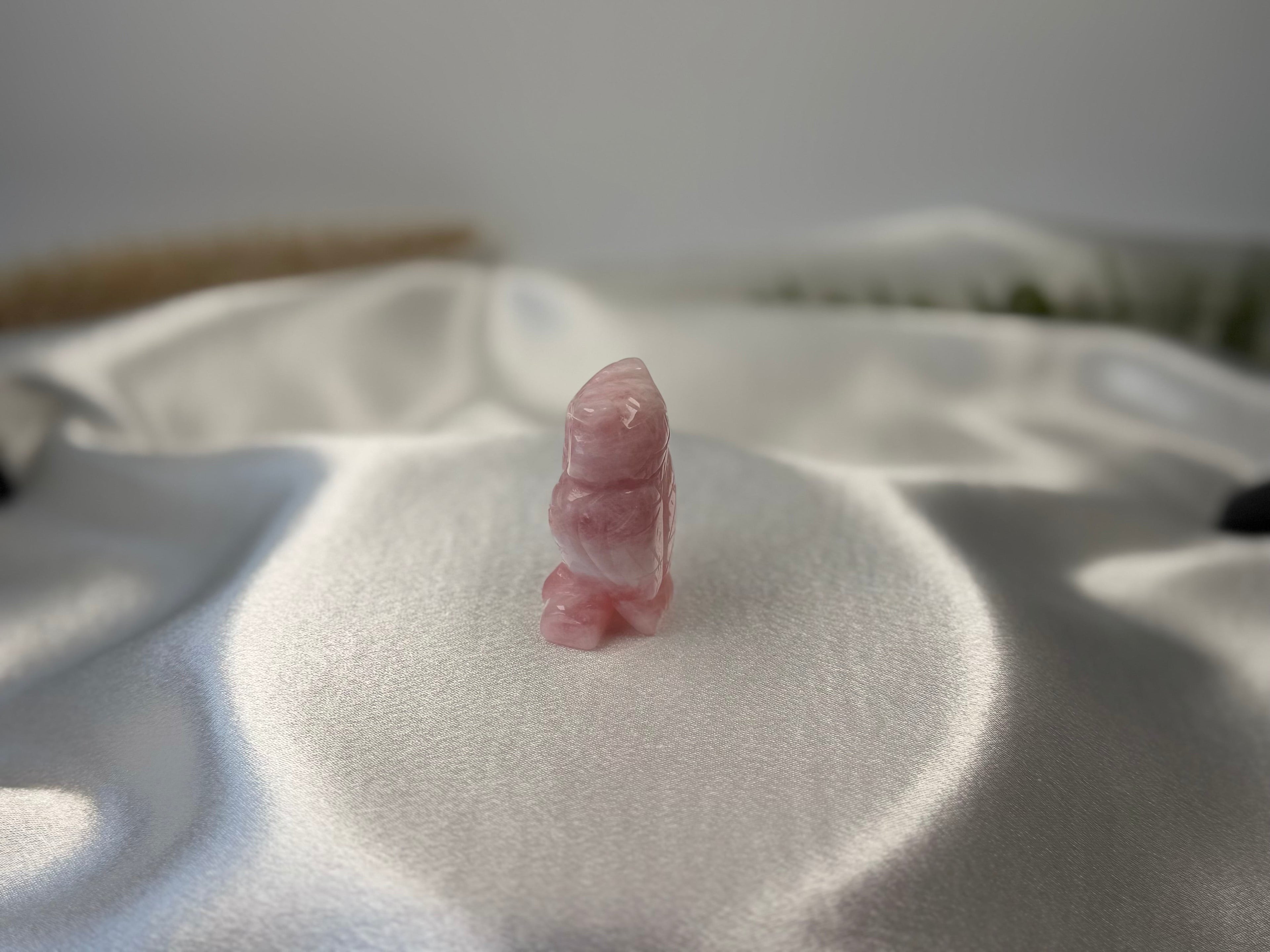 Treasured Energies rose quartz crystal owl carving with a smooth polished finish on a white satin background