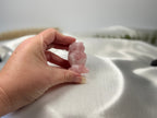 Treasured Energies rose quartz owl carving held in a hand against a soft white satin background.