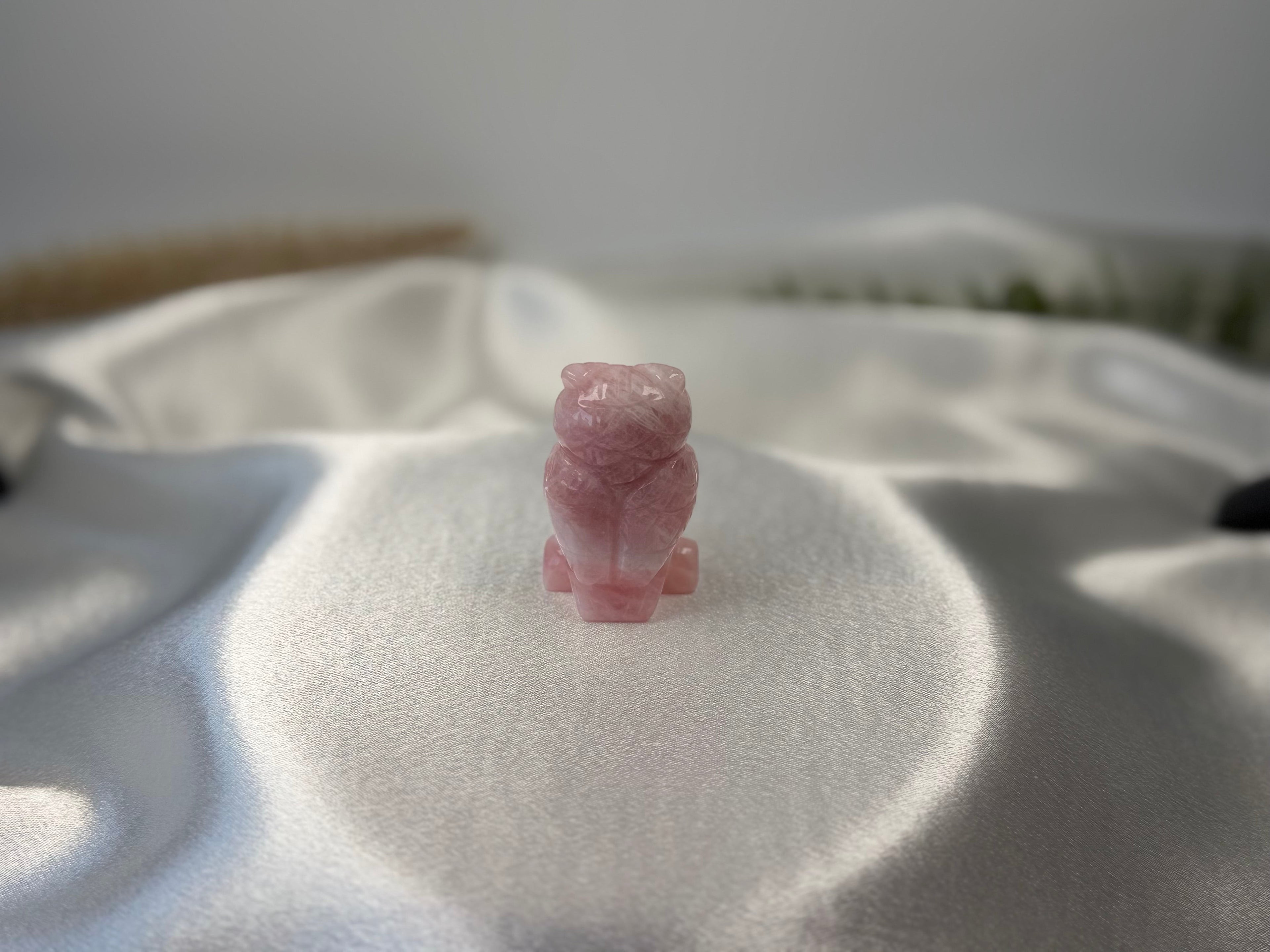 Treasured Energies rose quartz owl carving featuring a smooth, polished light pink crystal on a white satin background.