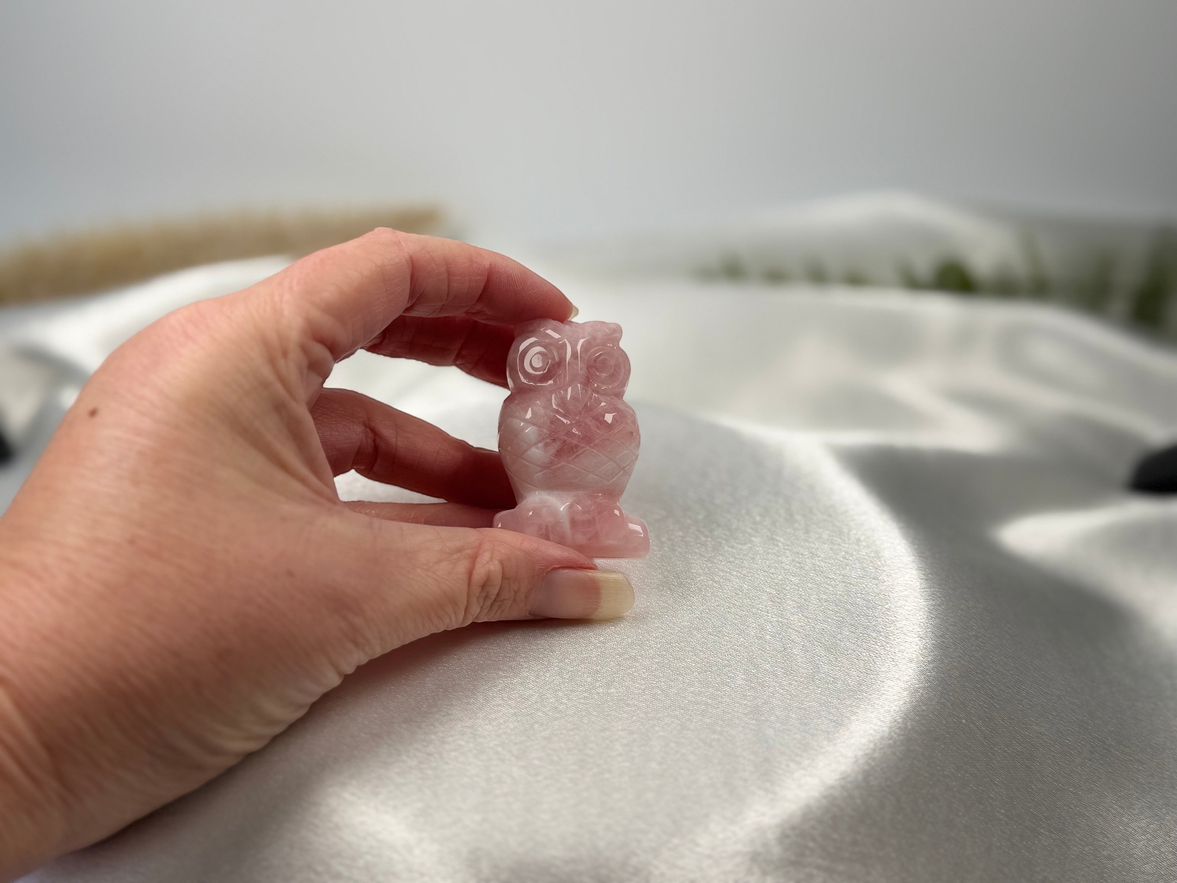 Treasured Energies hand-carved rose quartz owl figurine held against a soft white satin background.