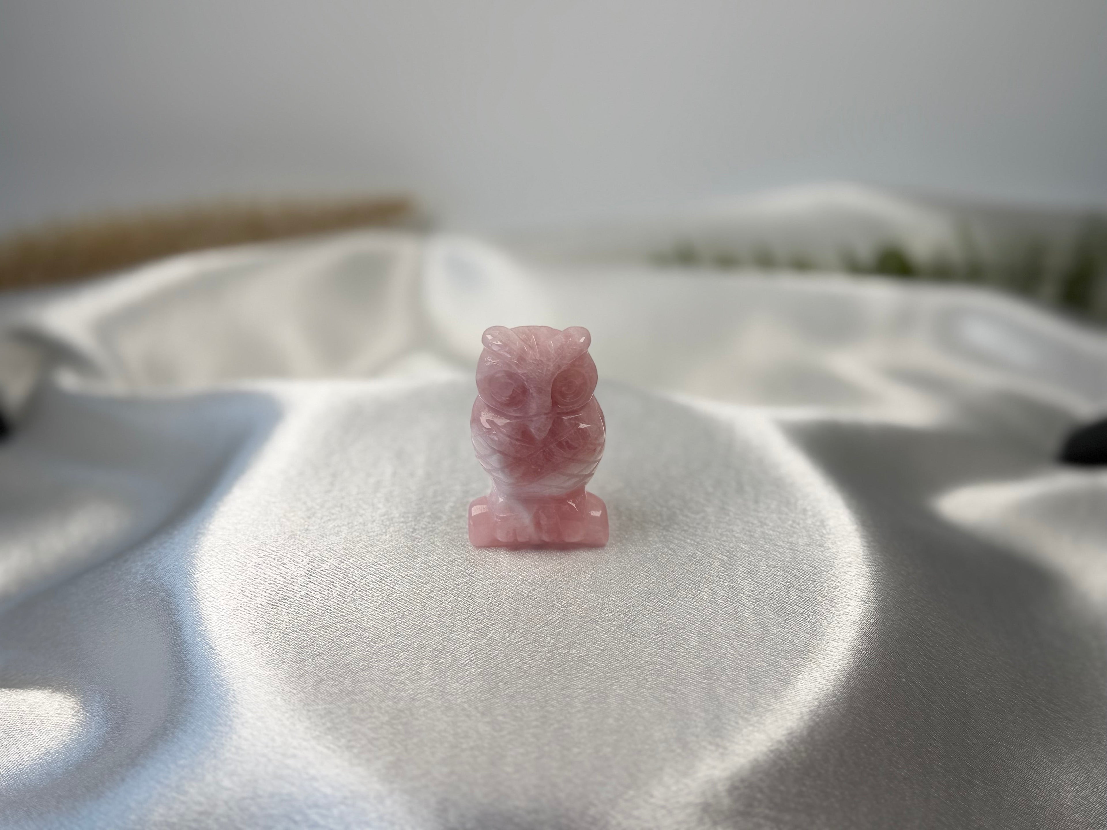 Treasured Energies rose quartz owl carving with a smooth, polished finish resting on a soft white satin fabric.