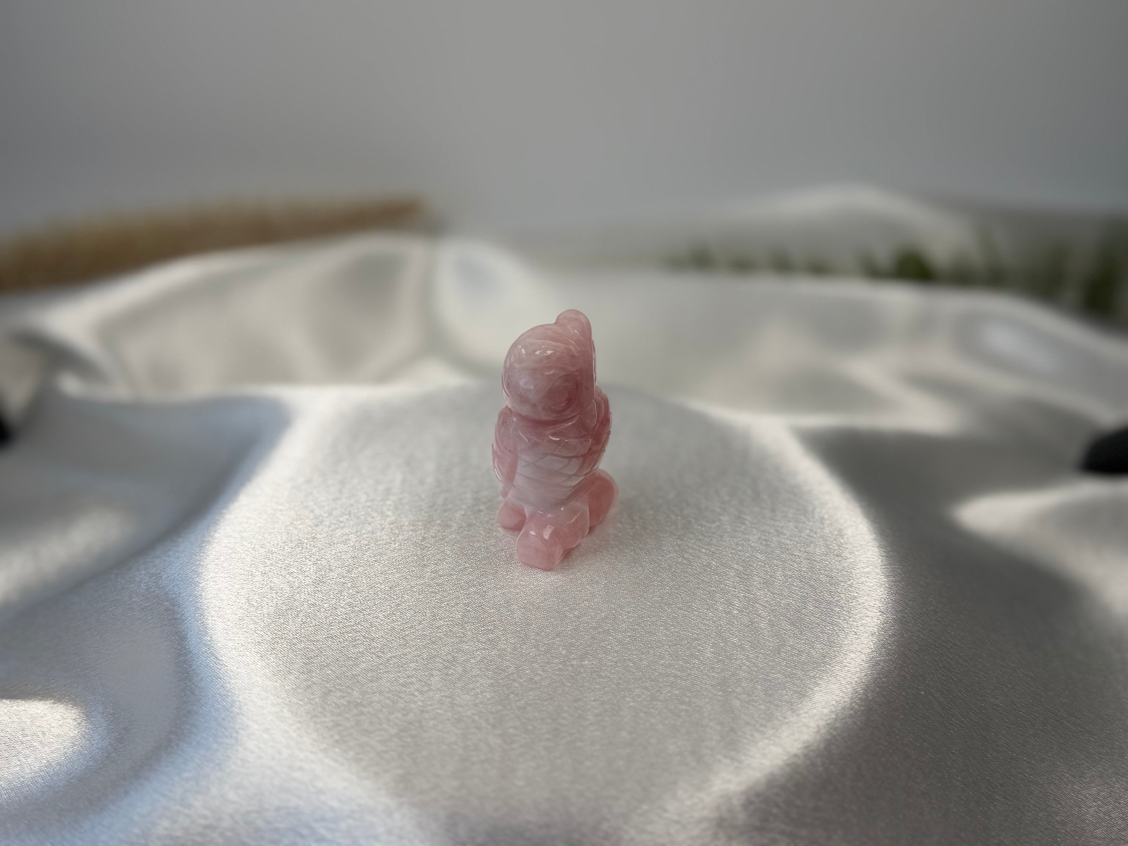 Treasured Energies rose quartz crystal owl carving resting on a smooth white satin fabric background