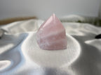 Treasured Energies medium rose quartz crystal point with a polished top and raw base on a white satin fabric background.