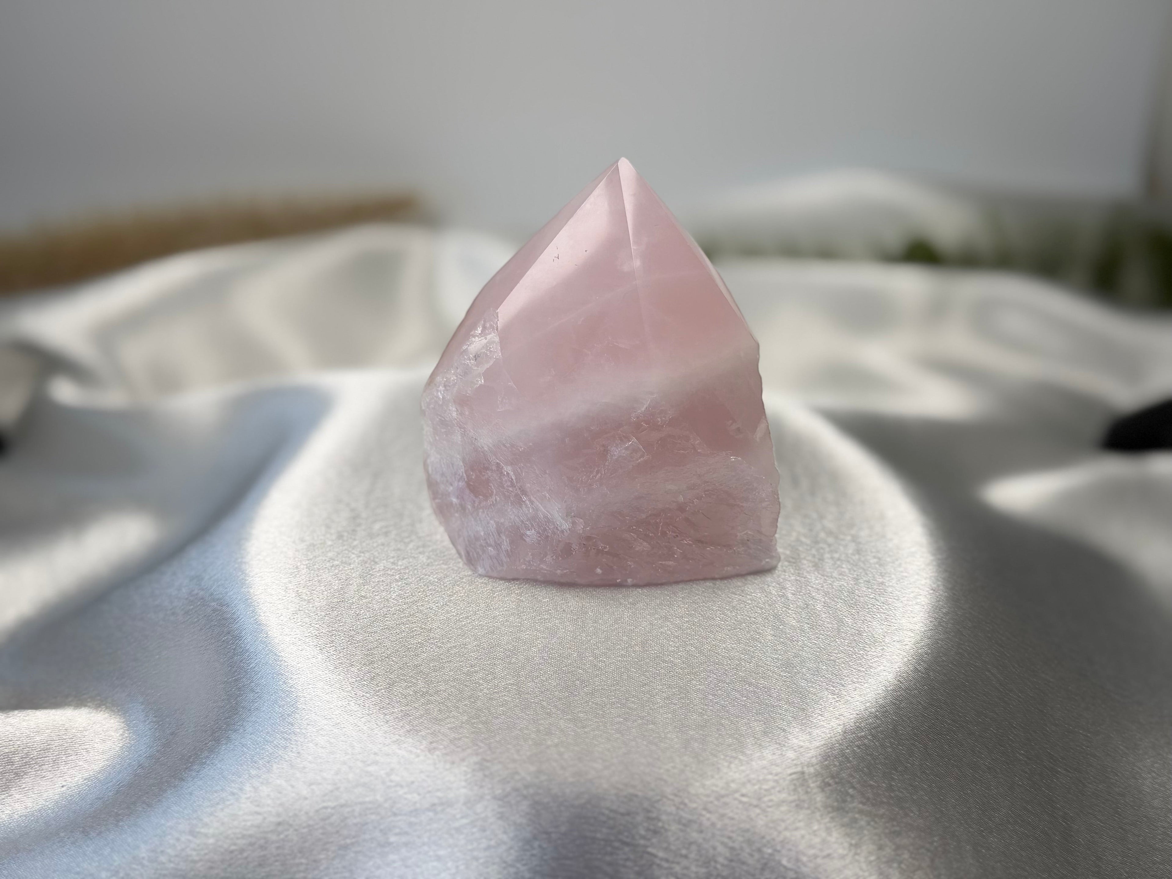 Treasured Energies medium rose quartz crystal point with a polished top and raw base on a white satin fabric background.