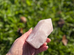 Treasured Energies large rose quartz crystal point with a polished tip and raw base held in a hand outdoors