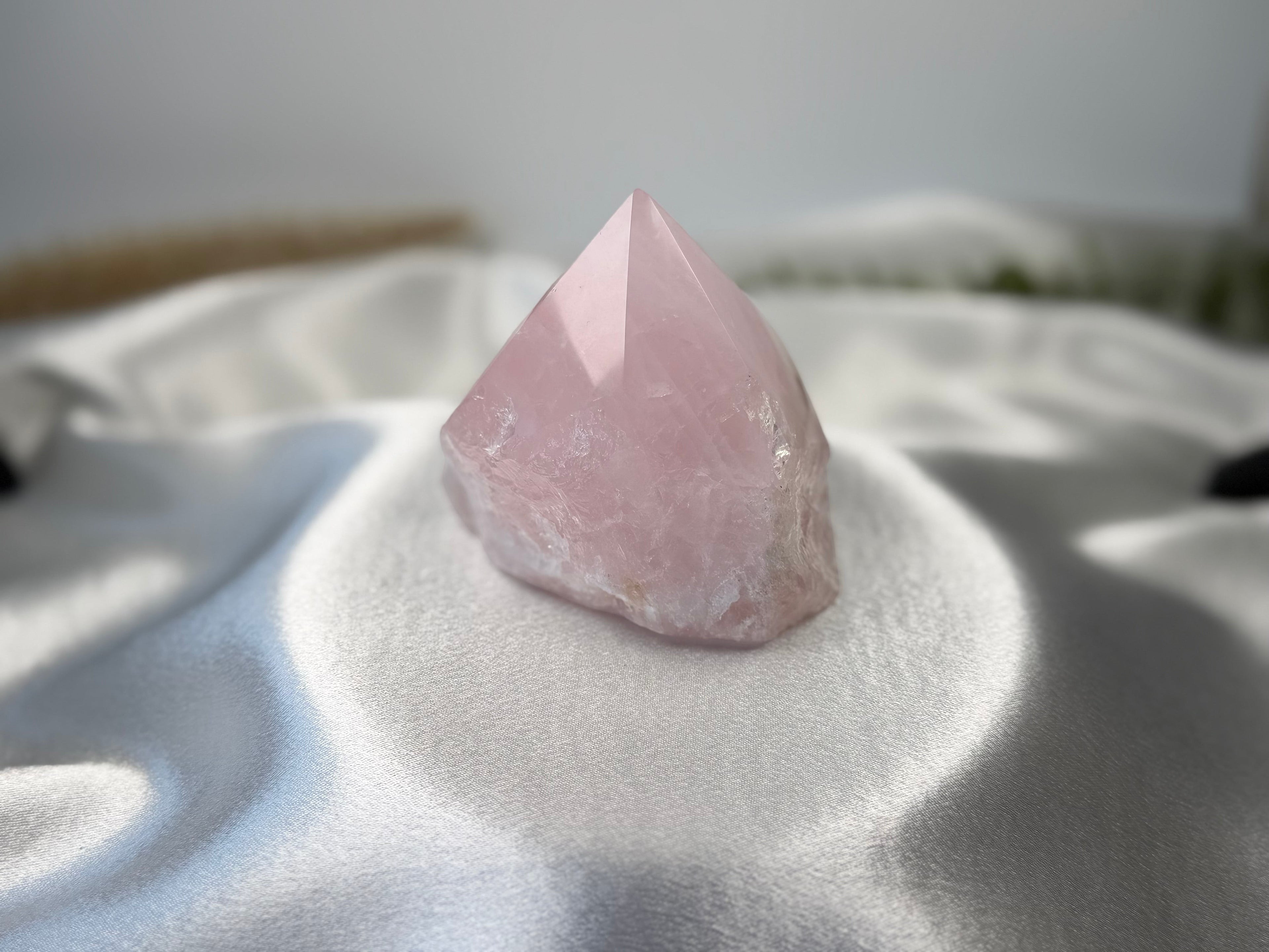 Treasured Energies medium rose quartz crystal point with a polished top and raw base on a white satin fabric background