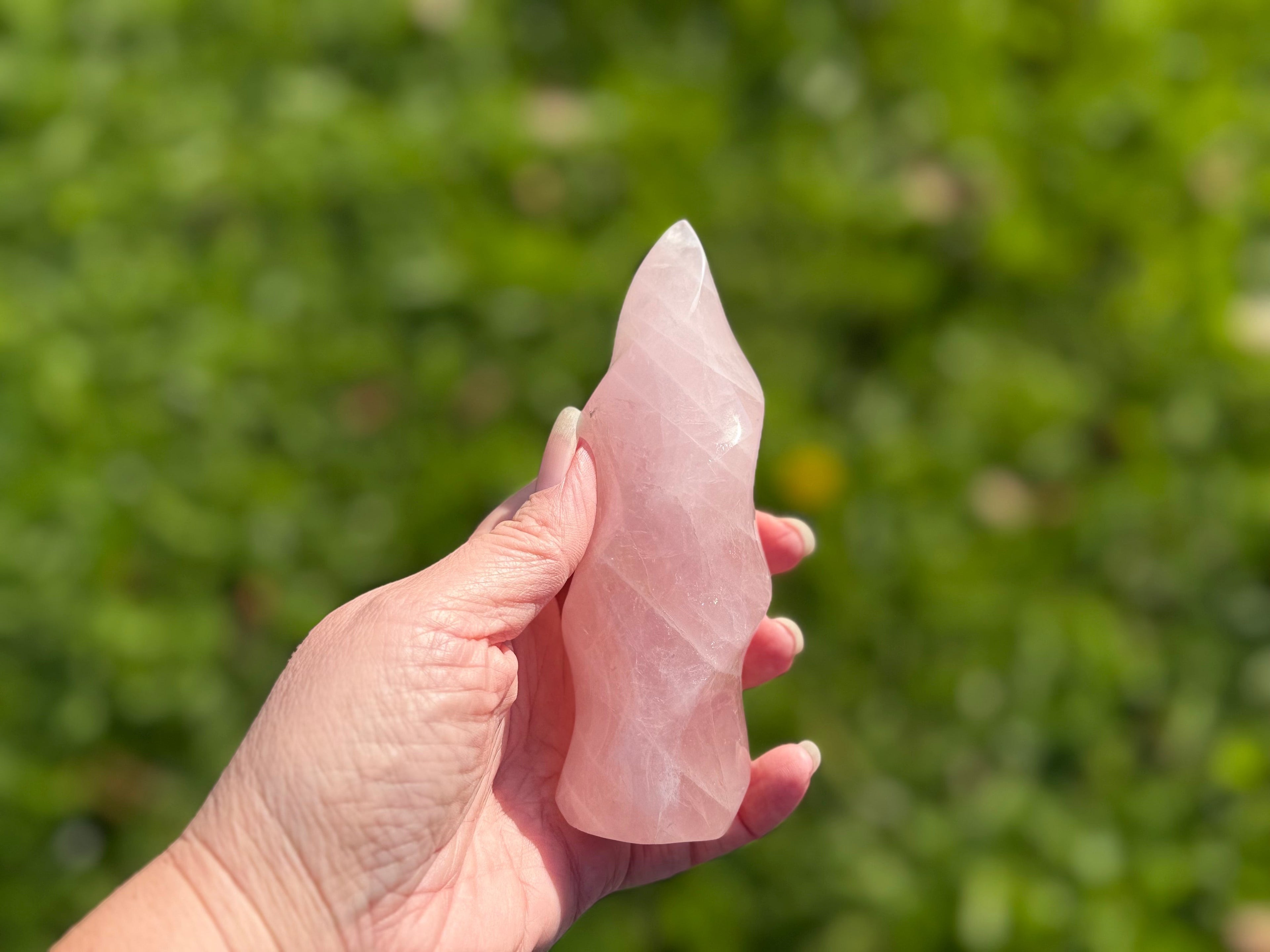 Treasured Energies large rose quartz crystal carved into a smooth, twisting spiral flame shape held in a hand.