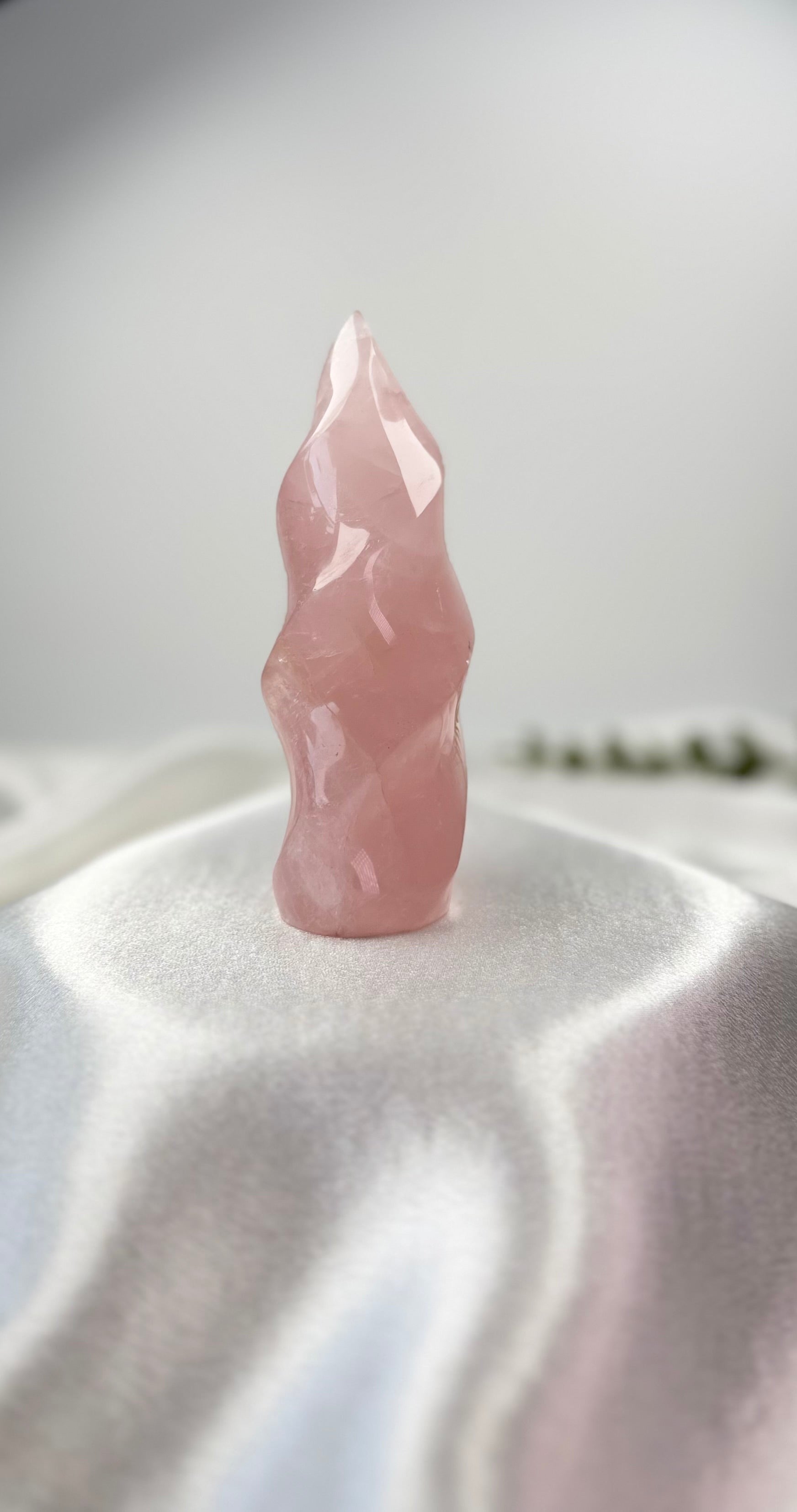 Treasured Energies large rose quartz crystal carved into a polished, twisting spiral flame shape on white satin.
