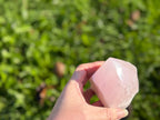 Treasured Energies medium rose quartz crystal tower with a polished point held in a hand against a green garden background