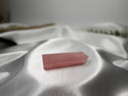 Treasured Energies polished rose quartz crystal tower point resting on soft white satin fabric